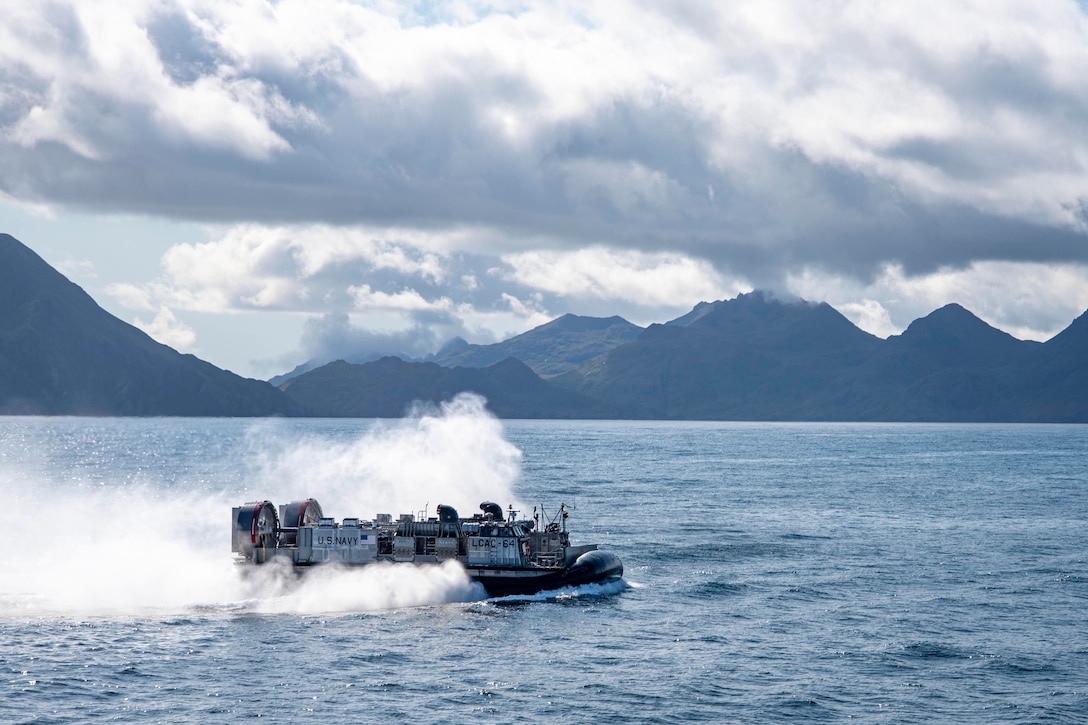 A air-cushioned landing craft travels through waters with mountains in the background.