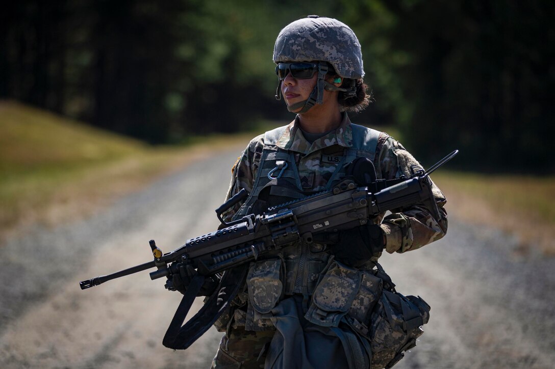 A soldier stands on a dirt road holding a weapon.