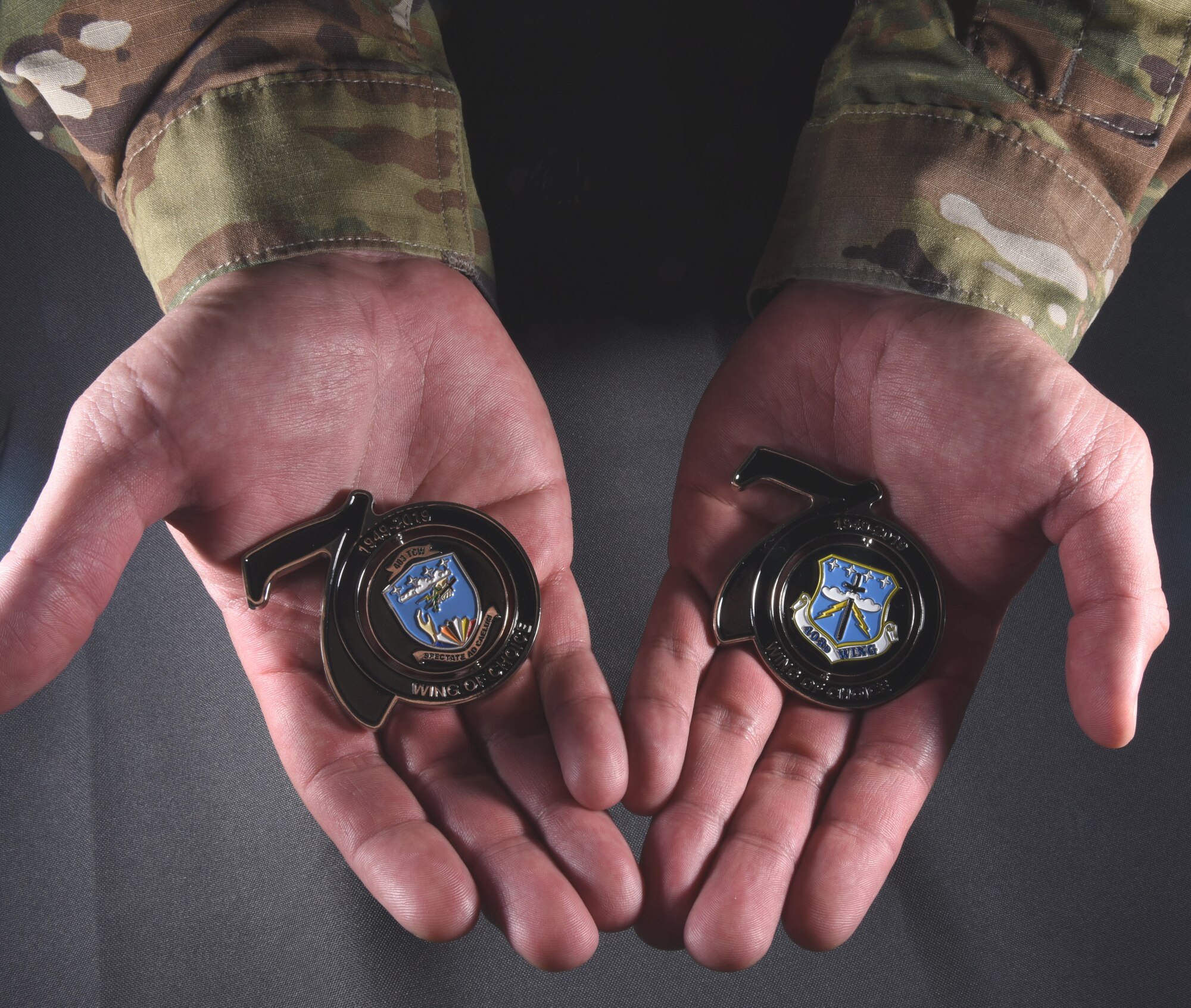 Tech. Sgt. Christopher Carranza, a public affairs specialist for the 403rd Wing at Keesler Air Force Base, Miss., displays the two sides of the wing's 70th anniversary coins. The chief's group within the unit designed the coins using the original 1953 shield and the present shield. (U.S. Air Force photo by Senior Airman Kristen Pittman)