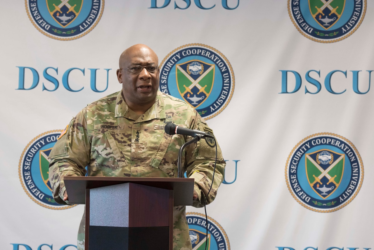 A uniformed service member speaks at a lectern. Behind him, the letters “DSCU” and a logo are on a backdrop.