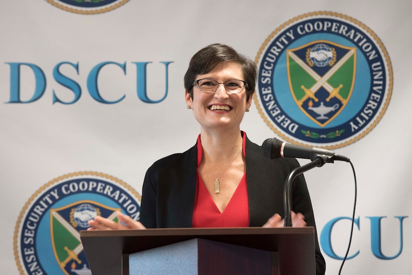 A woman speaks at a lectern. Behind her, the letters “DSCU” and a logo are on a backdrop.