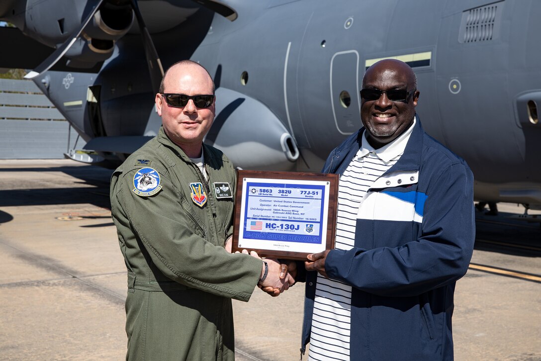 Photo of man presenting a plaque to another man in front of an aircraft