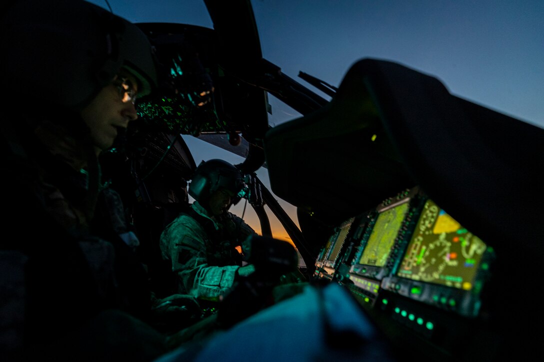 Service members sit in the dark cockpit of a military plane with bright monitors.