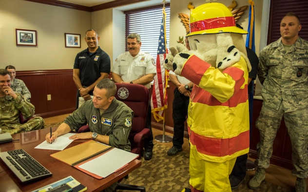 Col Lee Gentile, 47th Flying Traiining Wing commander, signs the Fire Prevention Week Proclamation as Sparky gives the "thumbs-up" Sept. 25, 2019 at Laughlin  Air Force Base, Texas. Gentile and base firefighters promoted the importance of fire saftey, as well as the upcoming FPW, which starts Oct. 7 - 11.  (U.S. Air Force photo by Master Sgt JT May III)