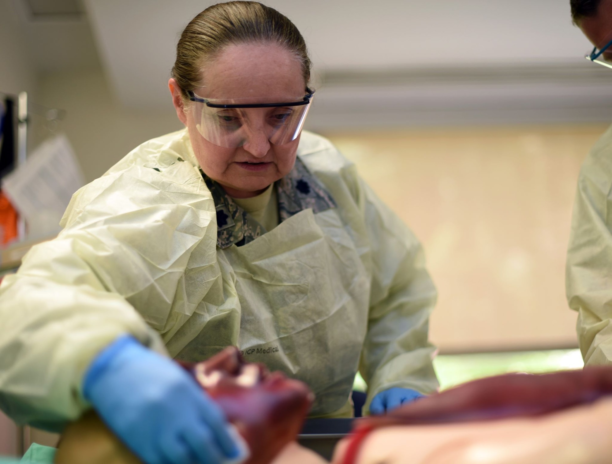 A female medical professional with latex gloves wipes gauze along the skin of a training mannequin. The training mannequin has rubber covering on it simulating a burn.