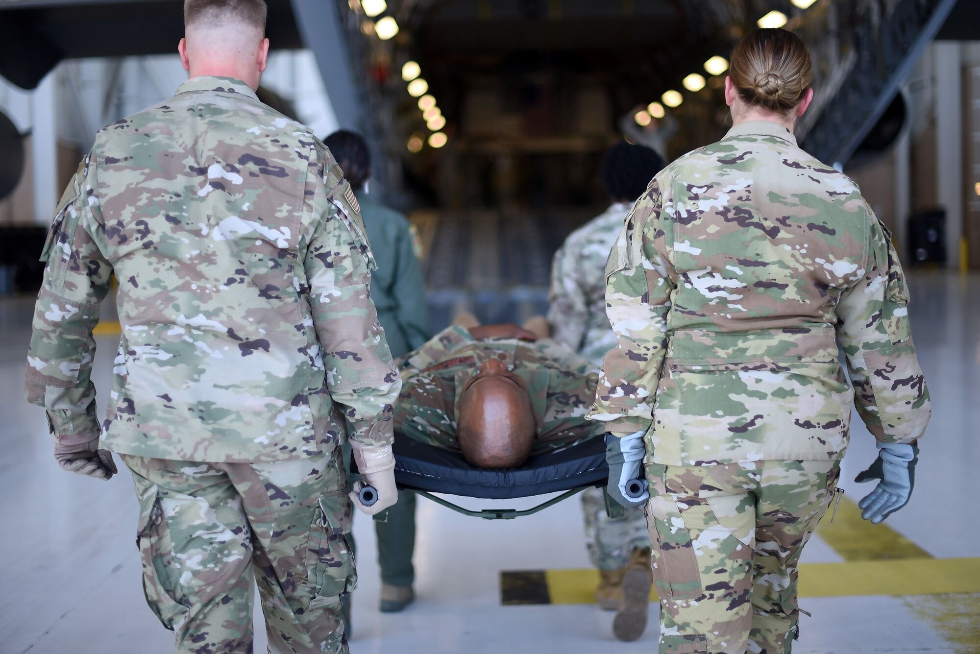 Chief Wright is carried in a stretcher by a group of four Airmen as they simulate evacuating injured people via the opened back hatch of a C-5M Super Galaxy