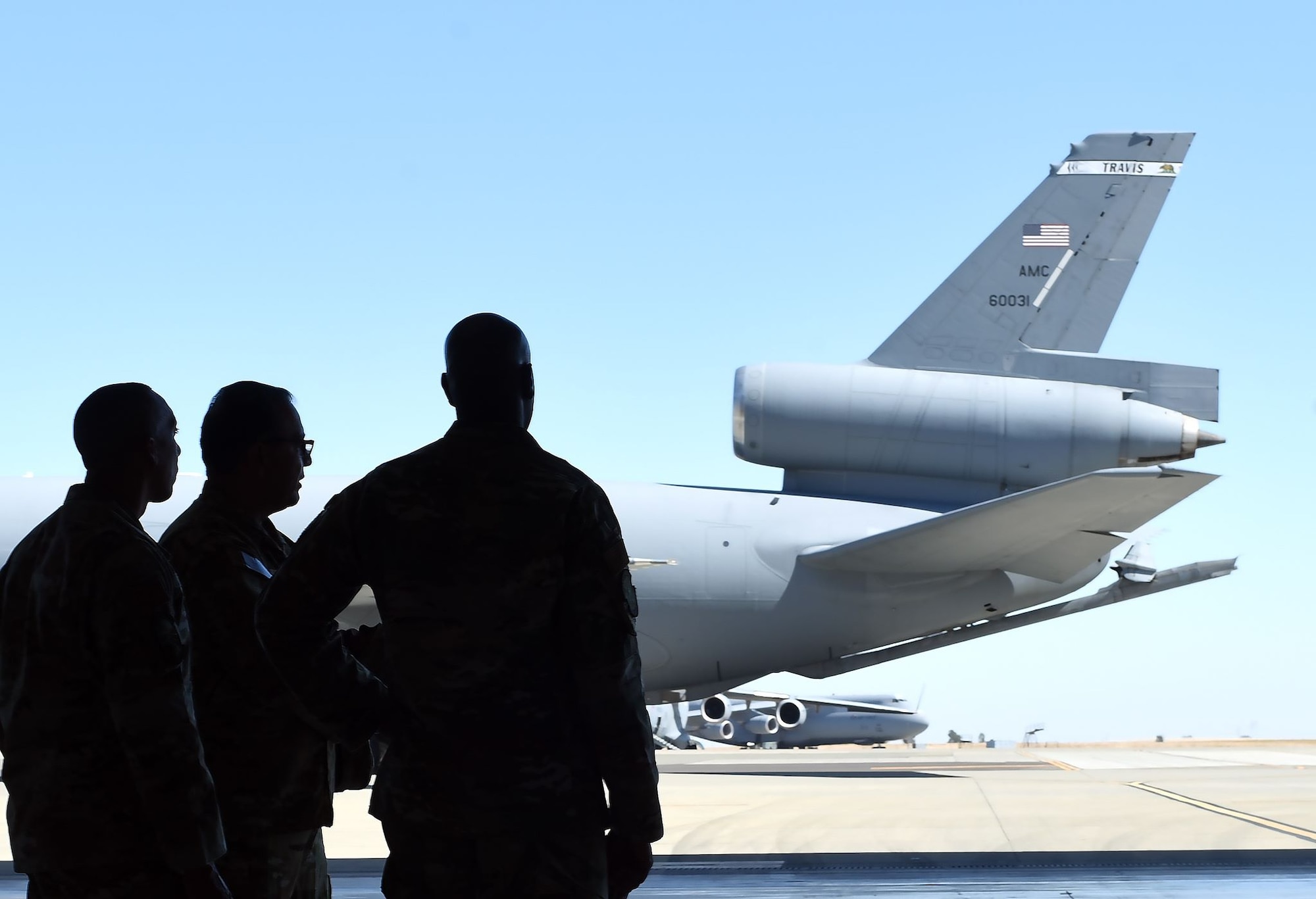 The forms of Chief Wright and two other Airmen are silhouetted against the bright light of the sun on the Travis flight line. Also pictured: the tail of a KC-10 Extender.