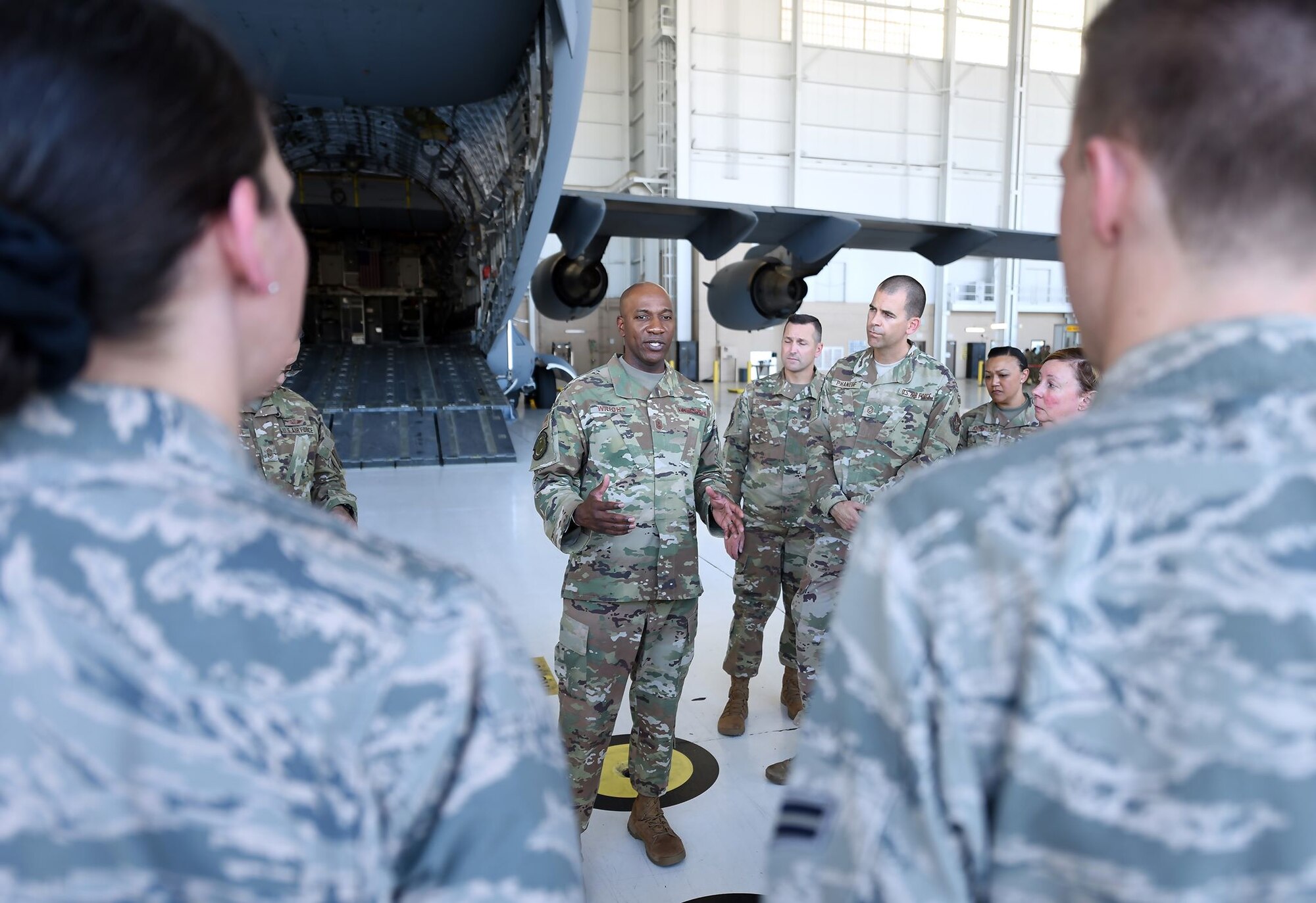 Chief Wright is surrounded by Airmen in an aircraft hangar. They're listening intently to what he's saying