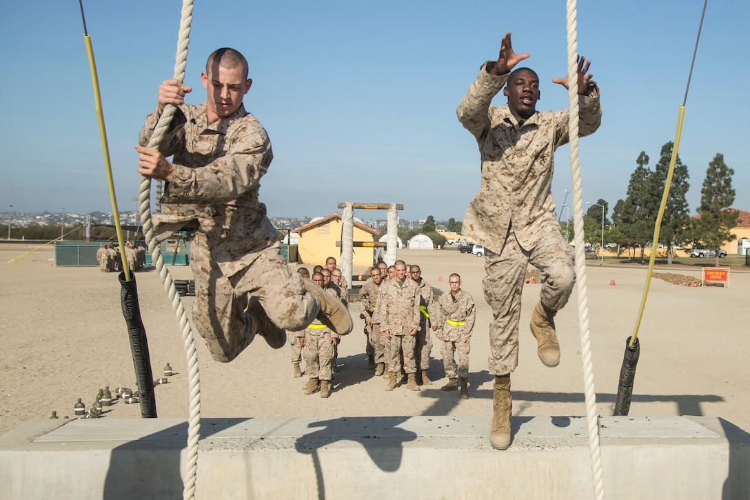 Marine Corps recruits swing on long ropes during a training course.