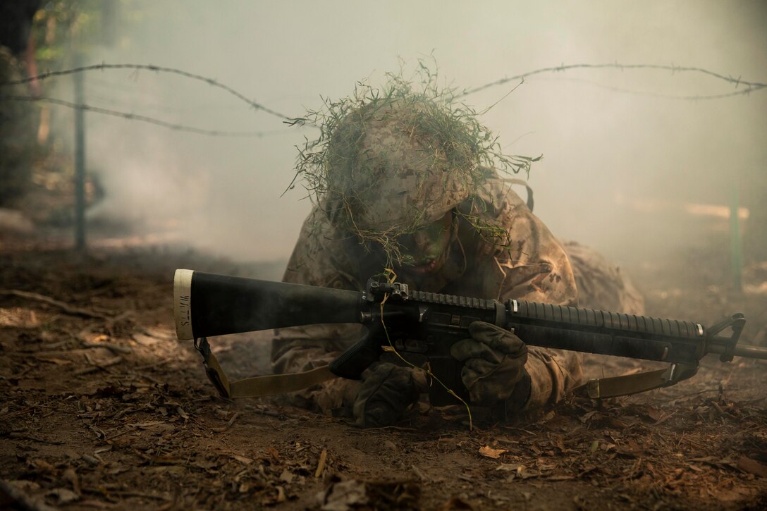 A Marine crawls under barbed wire.