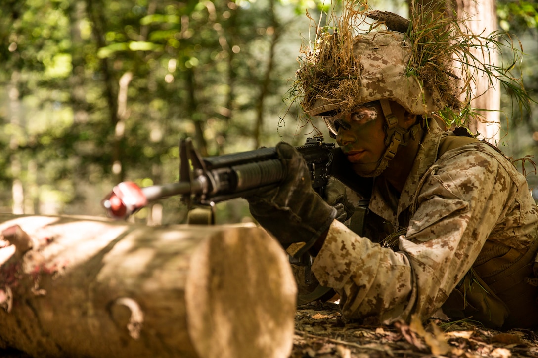 A Marine points his weapon from behind a log.