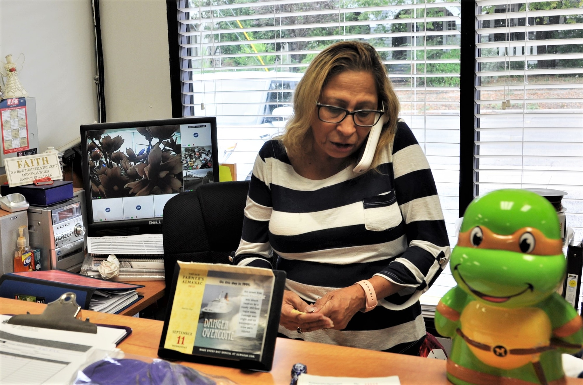 Mari Ayala Sandoval San Antonio, Texas Family Violence Prevention Services/Battered Women and Children’s Shelter’s Donation Center Coordinator, takes a call requesting items for a family leaving the shelter for their new home, during the Sept. 11 community outreach event at the San Antonio, Texas Family Violence Prevention Services/Battered Women and Children’s Shelter’s Donation Center. (background-striped top) opens the door to accept waiting donations. (U.S. Air Force photo by Janis El Shabazz)