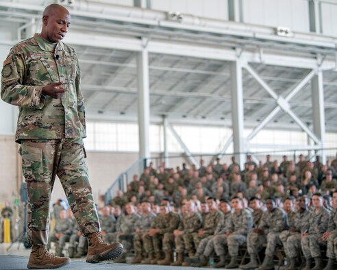 Chief Master Mgt. of the Air Force Kaltheth O. Wright stands in front of and talks to U.S. Airmen sitting in bleachers.