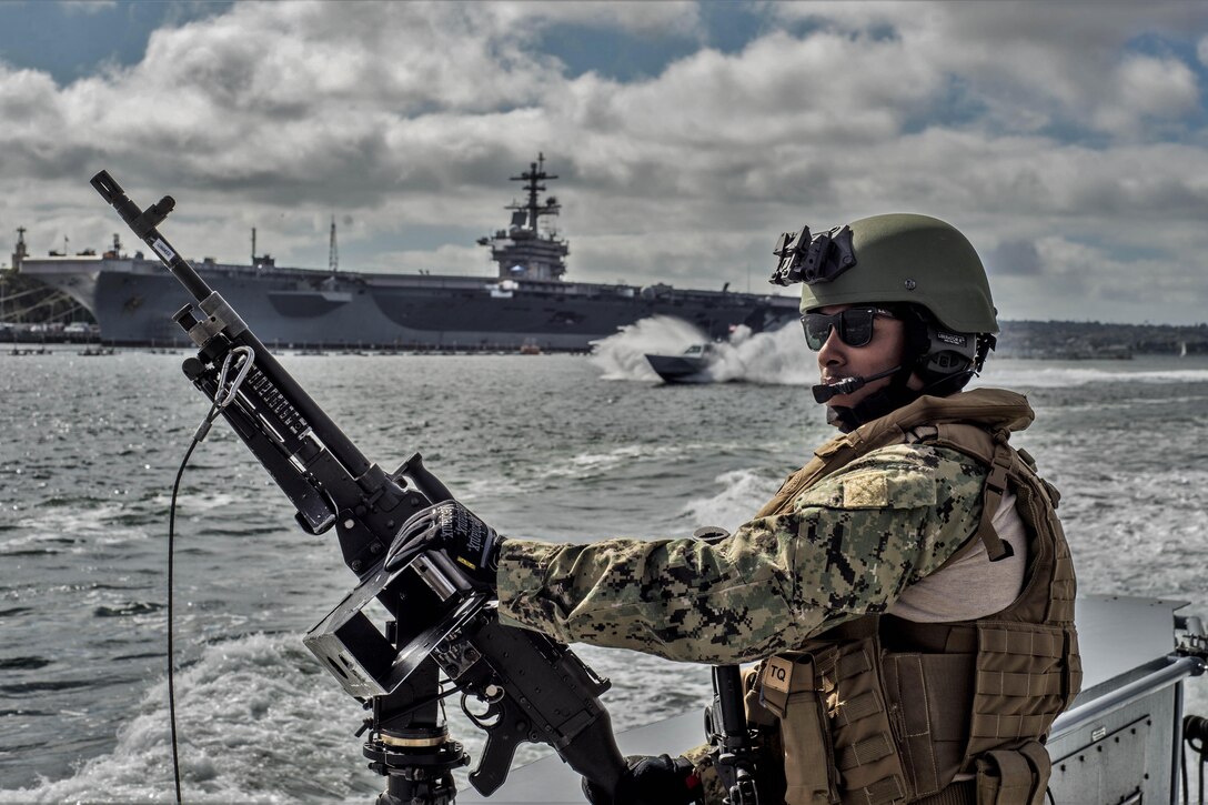 A sailor mans a machine gun on a boat across from a ship.