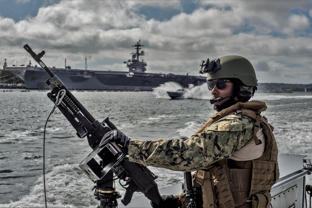 A sailor mans a machine gun on a boat across from a ship.