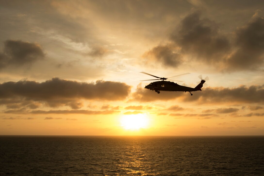 A helicopter flies over the ocean sunset.