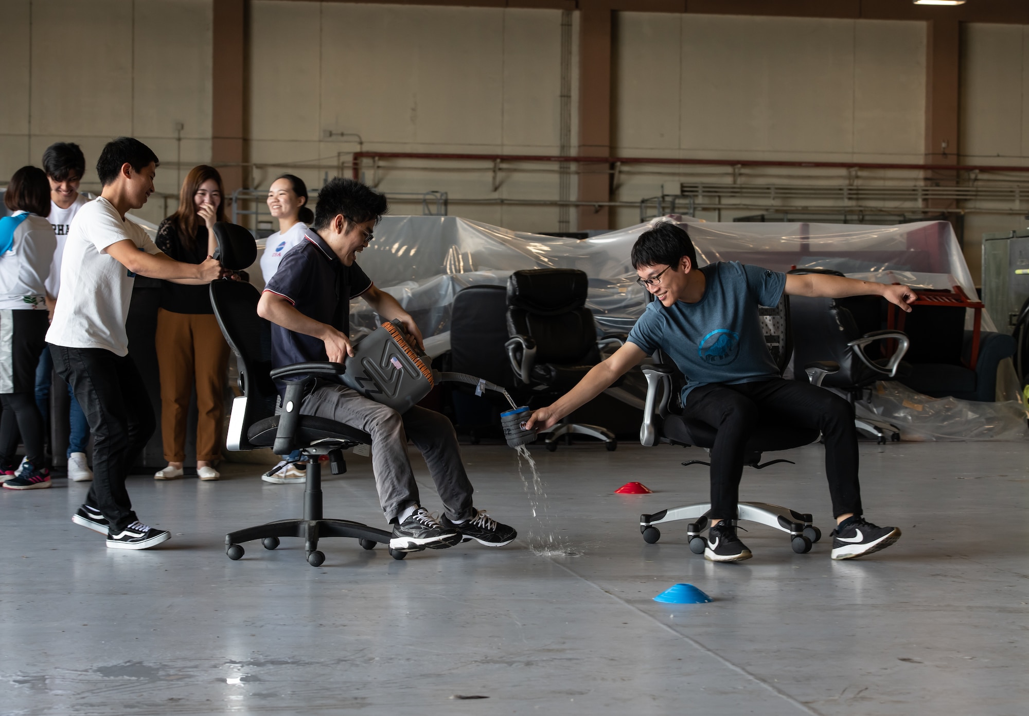 University students participate in an interactive challenge during Air Force Immersion Day, Sept. 23, 2019, at Kadena Air Base, Japan. The challenge was designed to give students a better understanding of aerial refueling by having one student act as the pilot of a KC-135 Stratotanker by pulling another student, the boom operator, in an office chair while a third student follows and attempts to have their cup filled by the boom operator. (U.S. Air Force photo by Staff Sgt. Micaiah Anthony)