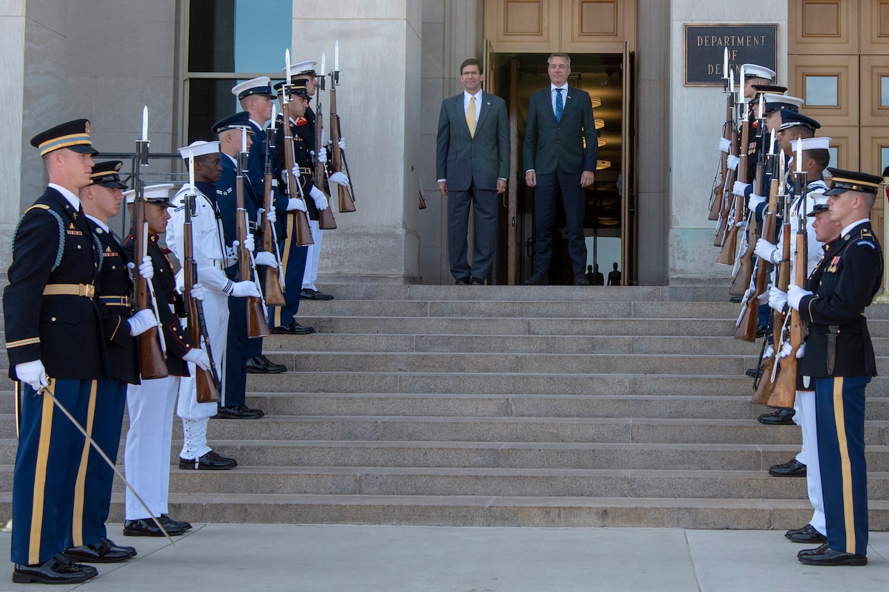 Two men stand at the top of Pentagon steps lined by an honor guard of uniformed service members.