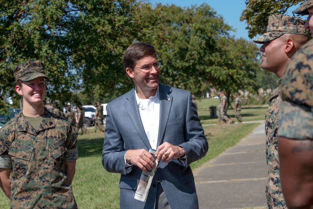 Defense Secretary Dr. Mark T. Esper smiles and talks with several smiling Marines on a sidewalk.