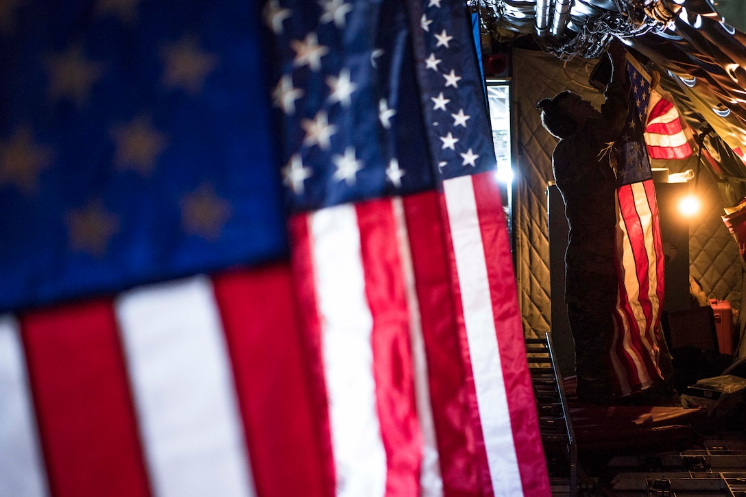 An airman hangs an American flag inside an aircraft with other flags hanging around.