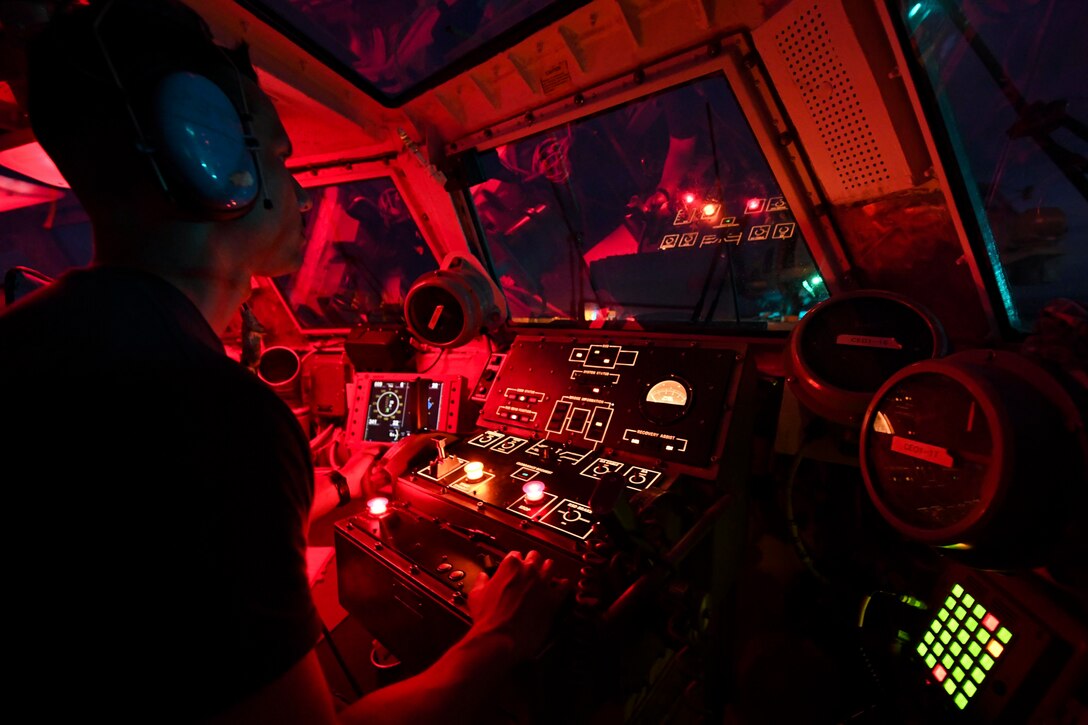 A sailor sits inside a ship while operating a console.