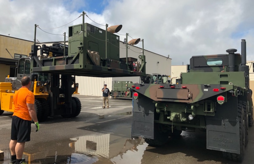 Photo of sheet metal mechanic helping install a power equipment group pallet onto a tactical vehicle.