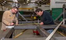 Photo of Welder and Welding Worker measure the PEG pallet frame assembly to mark the location of the cross beam.