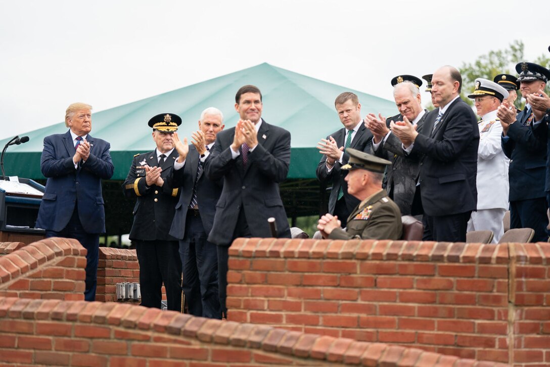 A group of people stand clapping as one man sits.