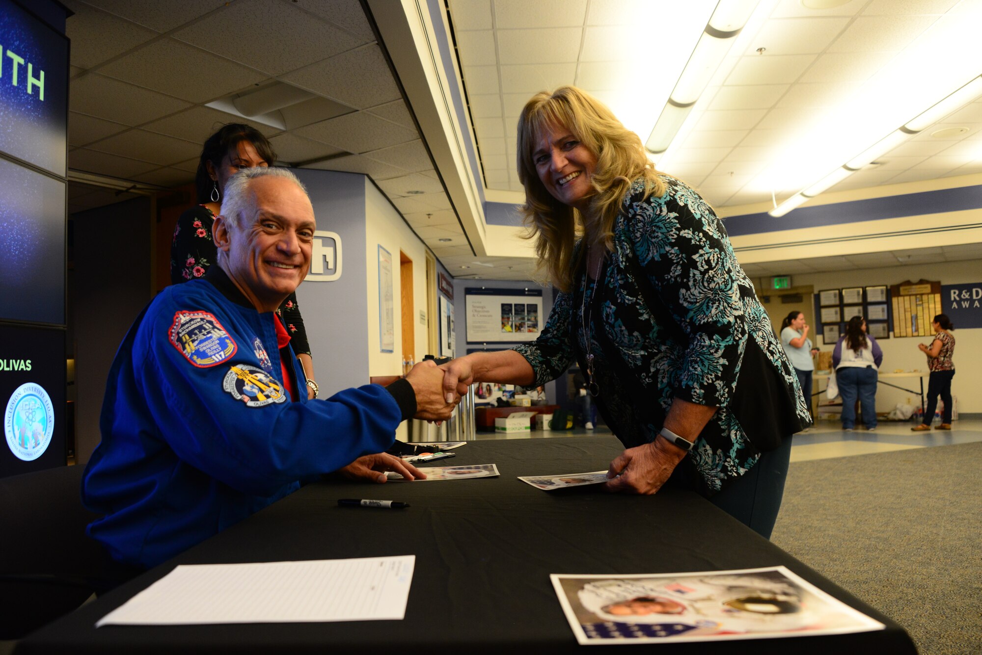 John Olivias, an American engineer and a former NASA astronaut, shakes hands with Taunja Osborn, in the Steve Schiff Auditorium of Sandia National Laboratories on Sept. 25, 2019. Sandia hosted the event where participants sampled Hispanic foods, viewed and judged student artwork and listened to Olivias talk about his contributions, and journey with NASA. 
This was the first event to highlight Hispanic Heritage observance month on Kirtland. The month pays tribute to the contributions that Hispanics and Latino American culture have made to our nation. (U.S. Air Force photo by Jessie Perkins)