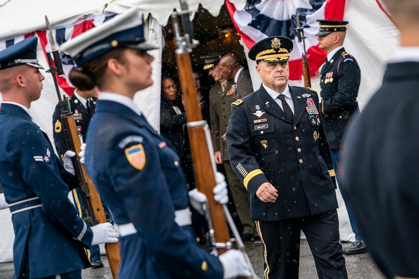 Army Gen. Mark A. Milley walks past honor guard troops on a rainy field.