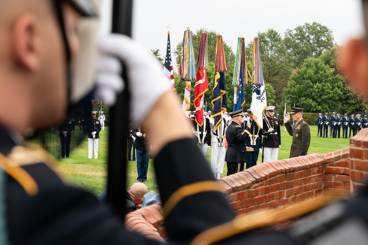 Marine Corps Gen. Joe Dunford and Army Gen. Mark A. Milley face each other on a field, their right hands raised; services members stand around.