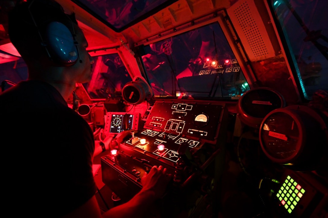 A sailor sits inside a ship while operating a console.