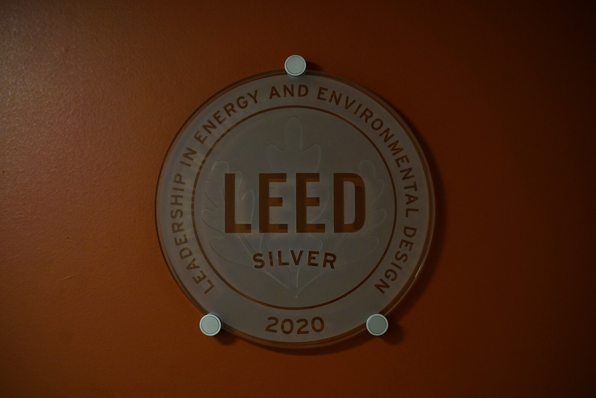A circular glass placard that reads "LEED Silver" hangs center-frame against a reddish-orange wall.