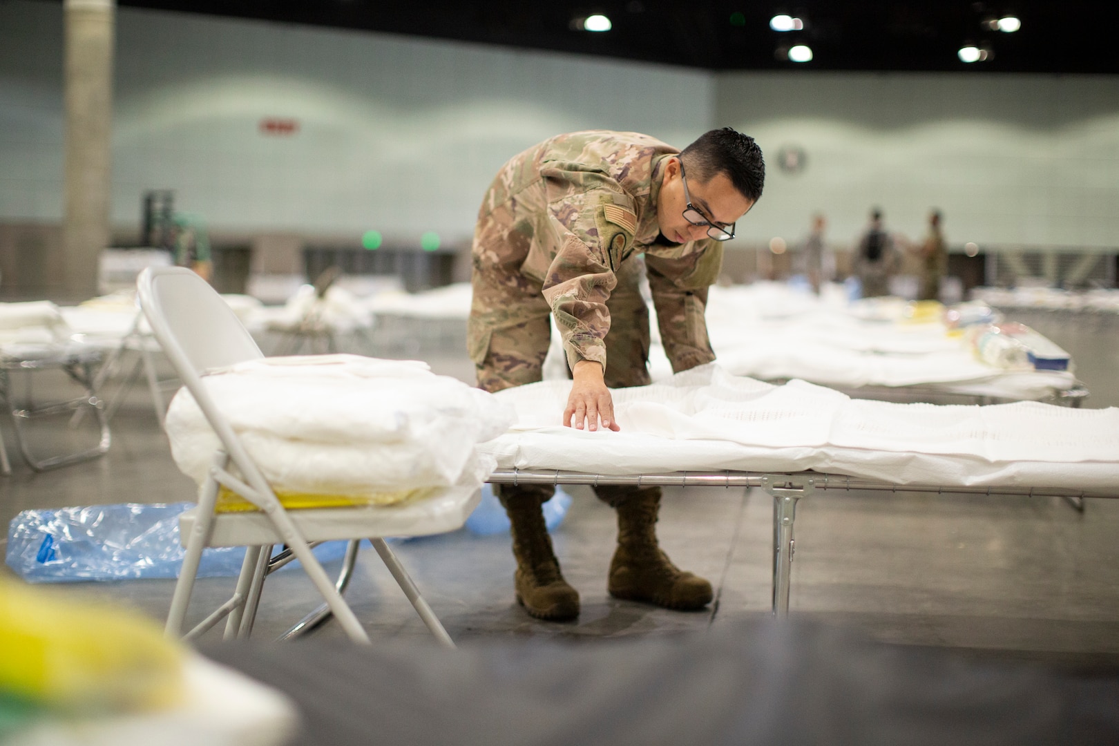 A male airman puts sheets on a  makeshift bed.