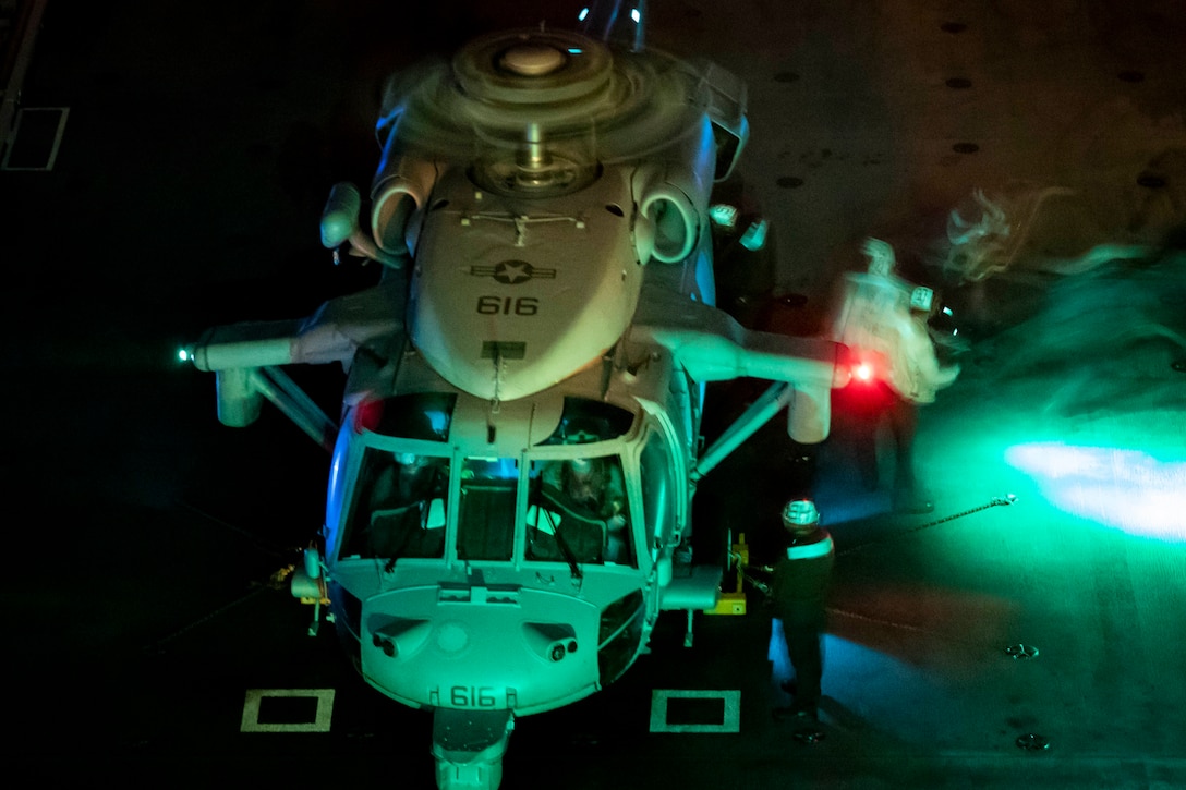 Sailors put fuel in a helicopter that is lit up at night.