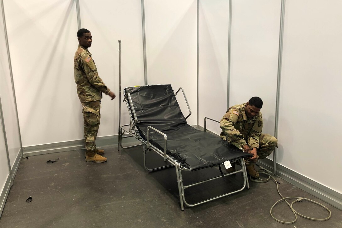 Two service members set up a cot.