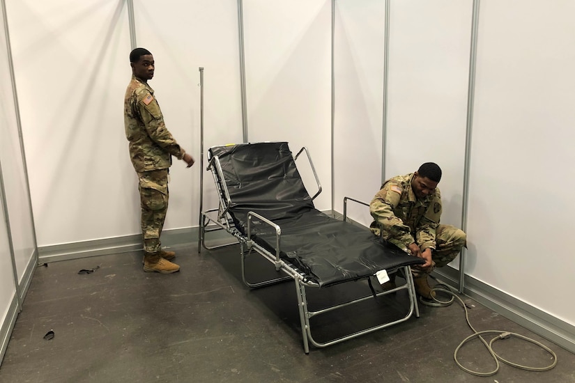 Two service members set up a cot.