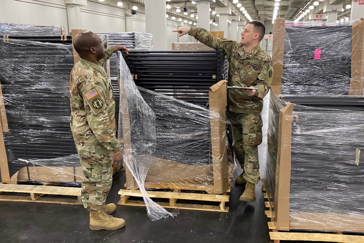 Two service members unwrap material on a shipping pallet.