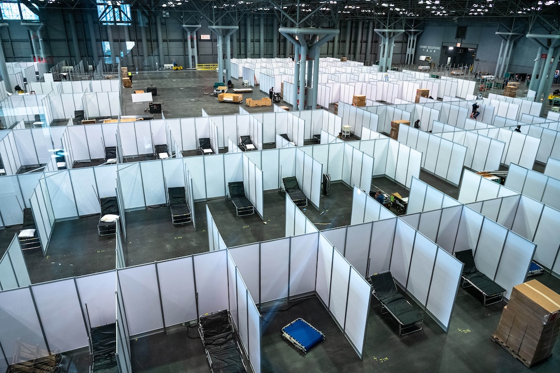 Dozens of partitions and cots are set up on a large convention center floor.