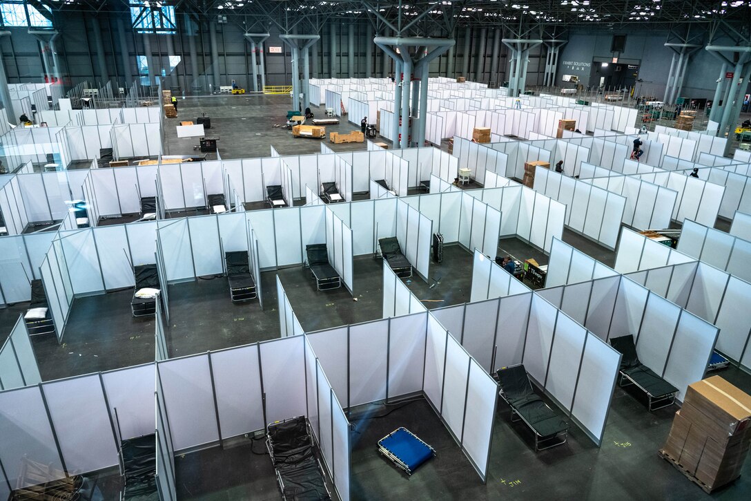 Dozens of partitions and cots are set up on a large convention center floor.