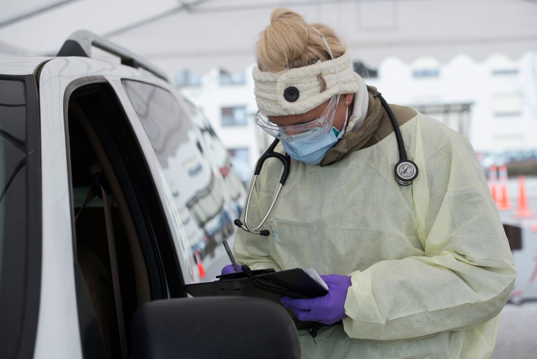 An airman dressed in personal protective equipment writes down medical information.