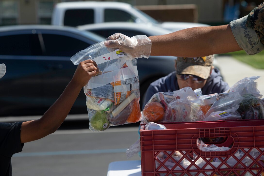 A U.S. Marine hands a child a bagged lunch at the San Onofre III Military Housing Community Center on Marine Corps Base Camp Pendleton, California, March 20, 2020. The Fallbrook Union Elementary School District and Oceanside School District are providing military students on base with bagged meals while schools are closed in response to the coronavirus outbreak. (U.S. Marine Corps photo by Lance Cpl. Andrew Cortez)