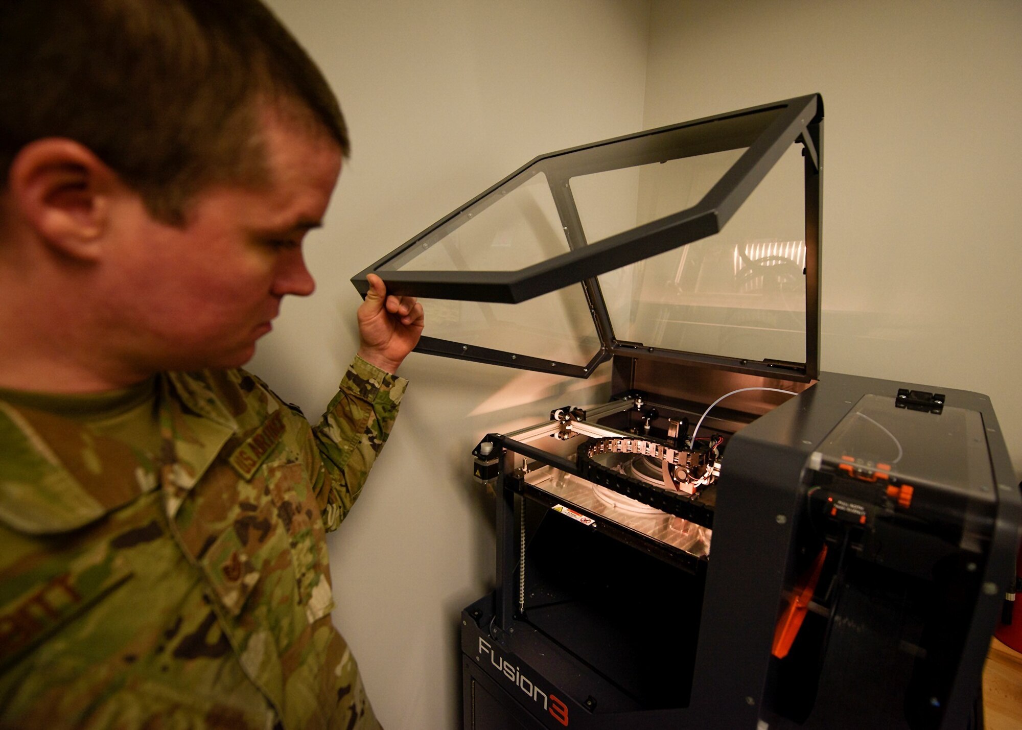 An Airman opens the cover to a 3D printer.