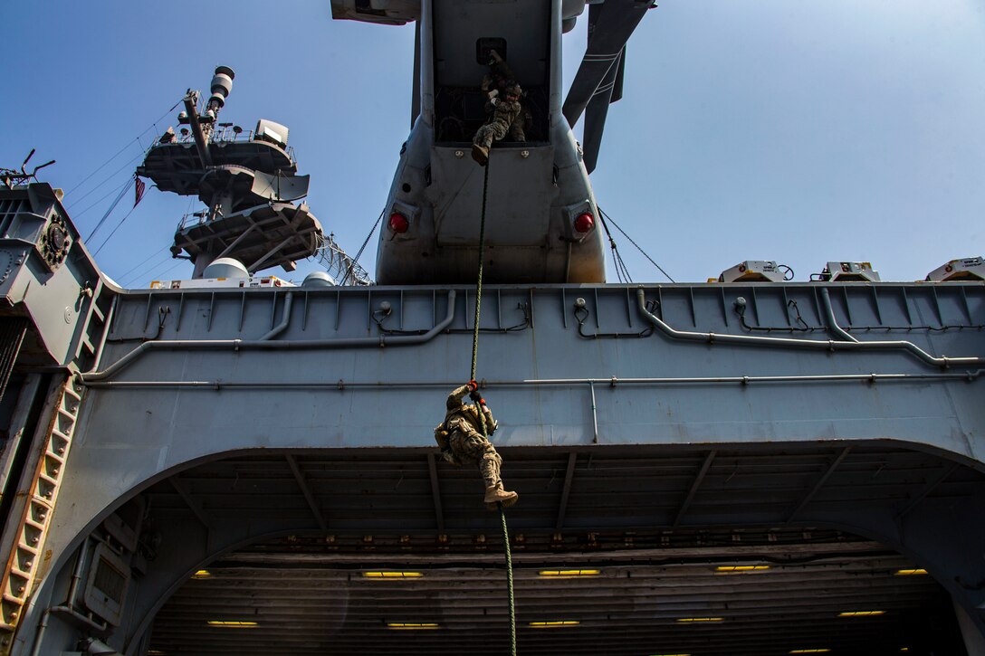 Marines rappel out of an aircraft.