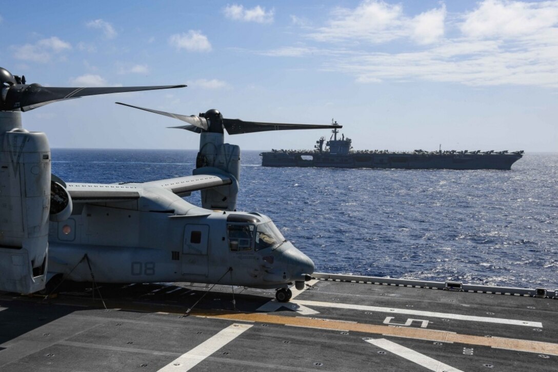 Tiltroter aircraft on the flight deck of a ship at sea, with another ship in the background.