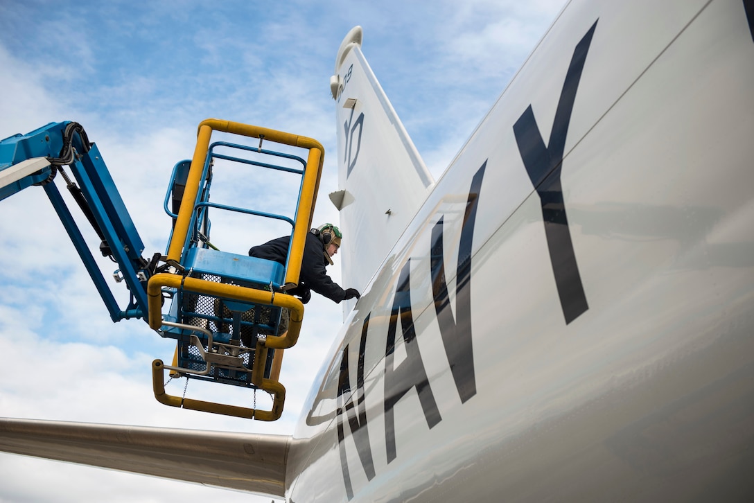 A sailor on an elevated platform inspects an aircraft.