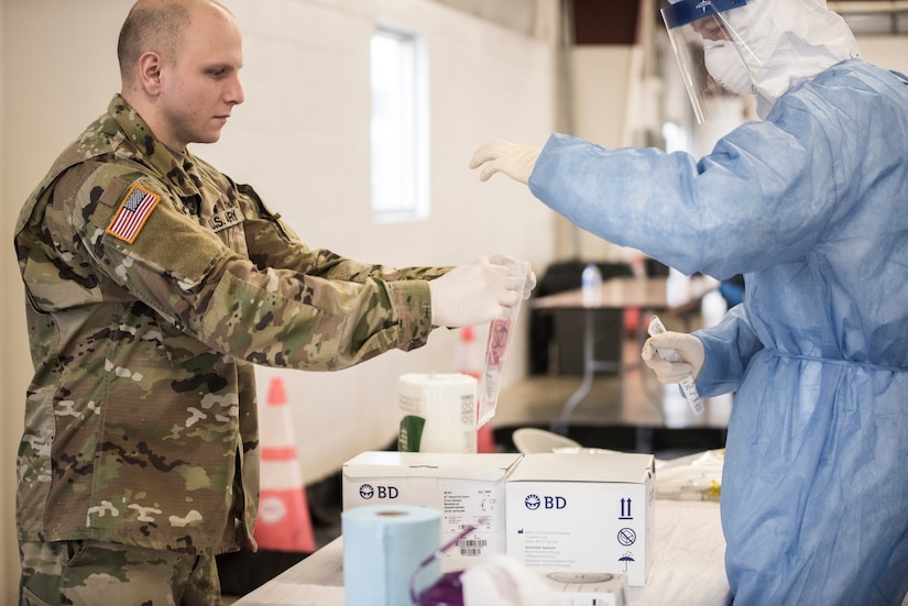 A person in uniform and a person in personal protective equipment bag a swabbed medical sample.