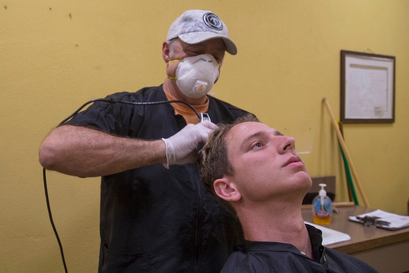 Masked barber gives recruit a haircut.