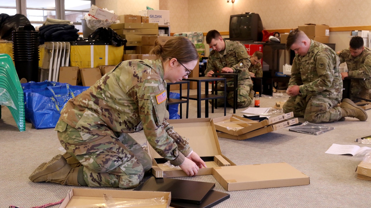 Soldiers kneel on a floor while assembling small tables.