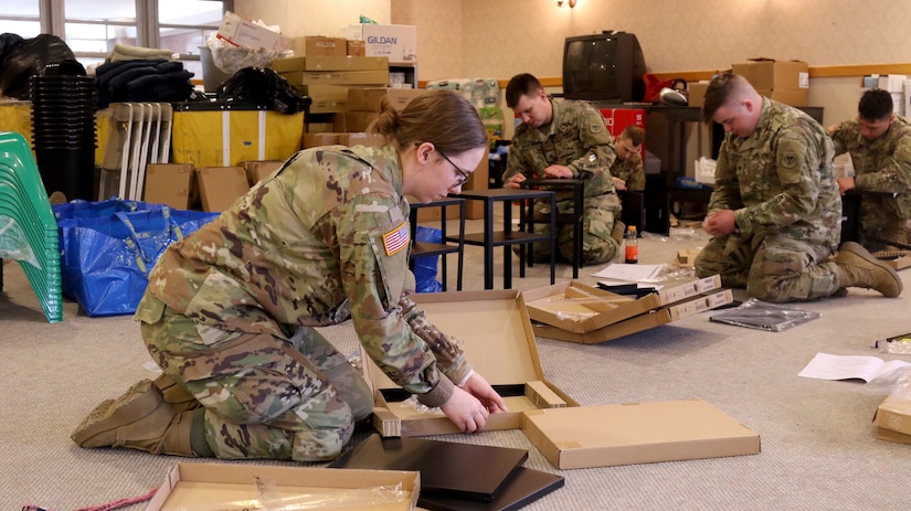 Soldiers kneel on a floor while assembling small tables.